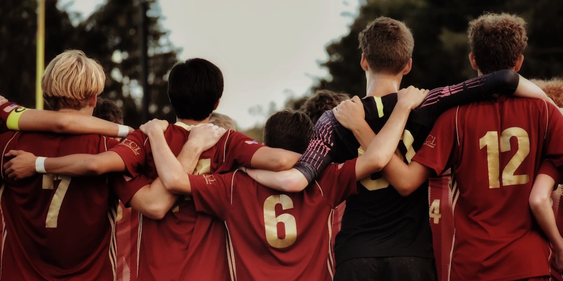 Chłopcy z drużyny piłkarskiej stoją obejmując się ramionami, sfotografowani od tyłu.